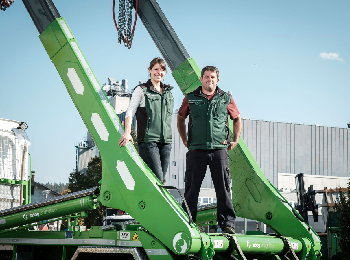 Judith Maag und Thomas Schwander stehen auf der Ladefläche eines Lastwagen mit hellgrünem UT-Absetzkipper als Aufbau. Industriegelände im Hintergrund.