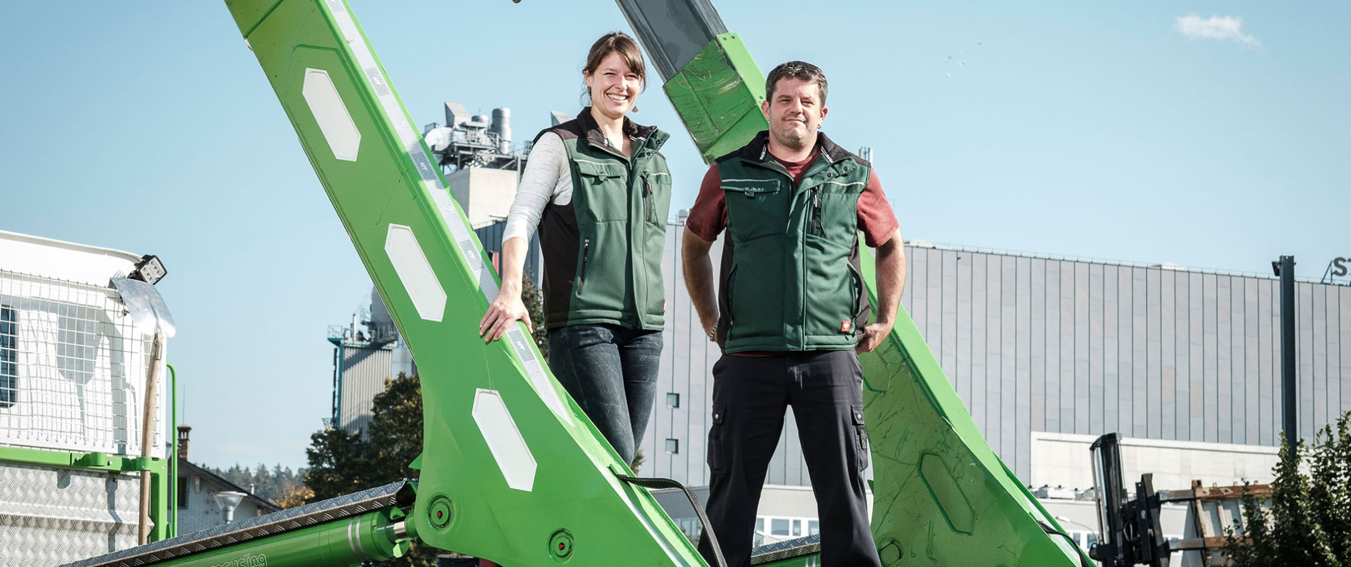 Judith Maag und Thomas Schwander stehen auf der Ladefläche eines Lastwagen mit hellgrünem UT-Absetzkipper als Aufbau. Industriegelände im Hintergrund.