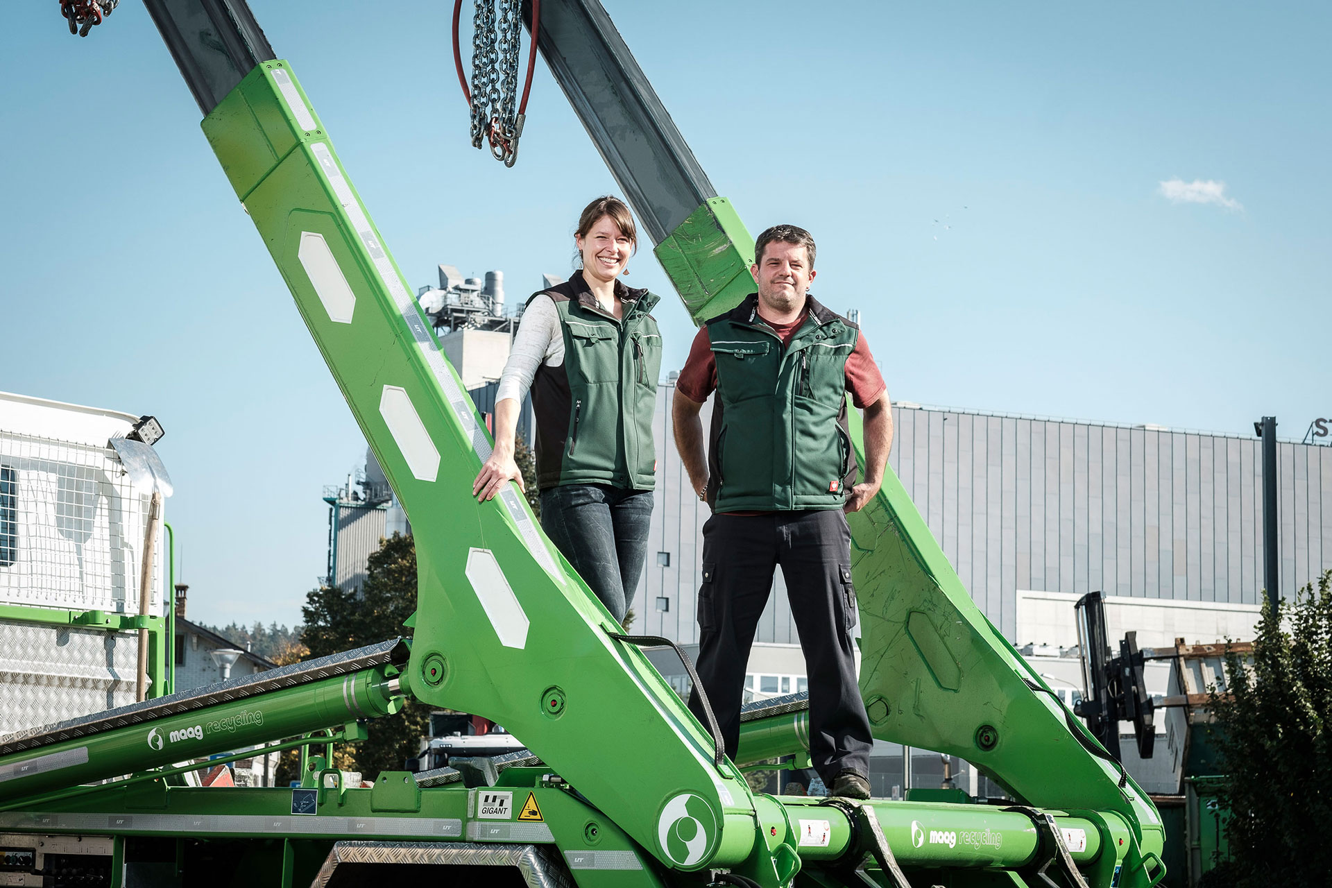 Judith Maag und Thomas Schwander stehen auf der Ladefläche eines Lastwagen mit hellgrünem UT-Absetzkipper als Aufbau. Industriegelände im Hintergrund.