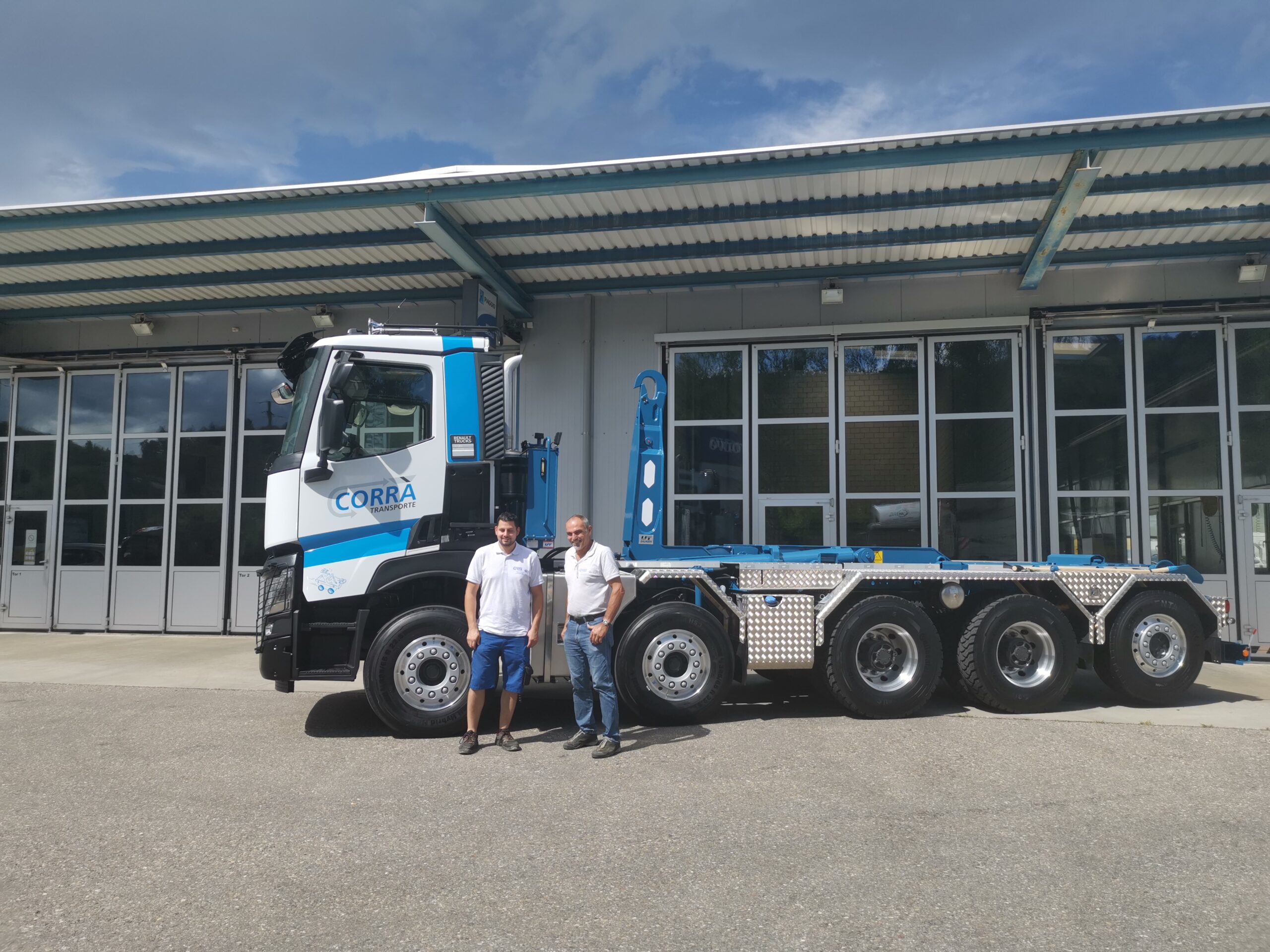 Nicola Corrà und Albert Corrà stehen vor ihrem Lastwagen mit dem neuen UT-Aufbau: Haken-Abrollkipper SAURIER 32TR80 VARITEC.
