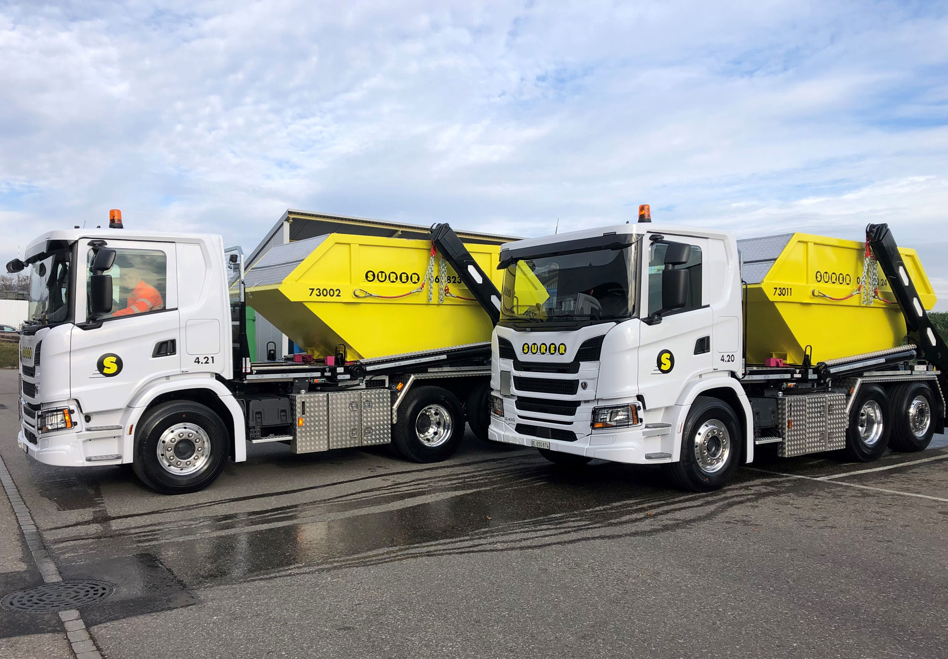 Zwei weisse Lastwagen mit gelben Mulden.